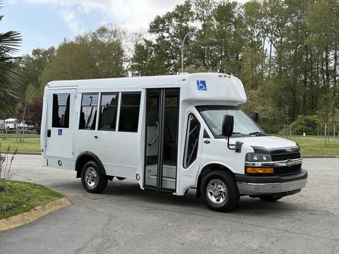 A white 2013 Chevrolet Express shuttle bus with wheelchair accessibility features and large windows
