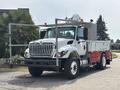 A 2012 International 7300 Workstar truck with a white and red body features a large flatbed and utility boxes on the sides along with a mounted equipment platform on the roof