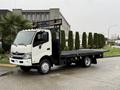 A 2015 Hino 195 flatbed truck with a white cab and black flatbed deck parked on a concrete surface