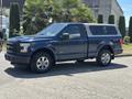 A Blue 2015 Ford F-150 pickup truck with a truck cap and chrome wheels parked on a paved surface