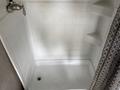 A clean, white shower stall with textured tiles and a chrome showerhead located on the left side is visible
