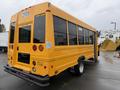 A yellow 2021 Ford Econoline bus with a rear door and multiple windows on the side visible