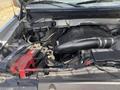The image shows the engine compartment of a 2014 Ford F-150 with a visible engine cover battery and various components and wiring