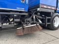 A 2013 International DuraStar 4300 with a large broom attachment positioned for street cleaning