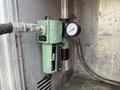 A green air pressure regulator with a gauge attached to a metal surface
