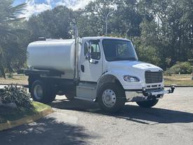 A white 2022 Freightliner M2 106 truck with a cylindrical tank mounted on the back and dual exhaust pipes on the side