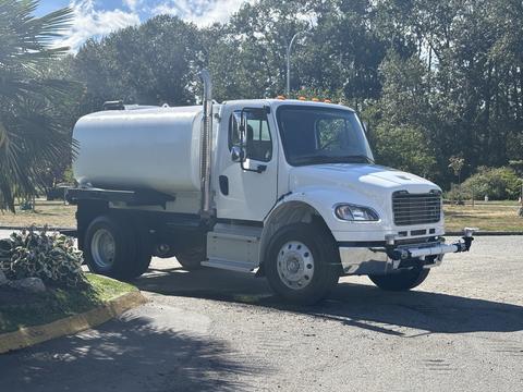 A white 2022 Freightliner M2 106 truck with a cylindrical tank mounted on the back and dual exhaust pipes on the side