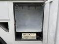 An open storage compartment of a vehicle showing a beige inverter labeled Dimensions and a gray shelf with hooks on the top wall