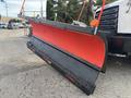 A snow plow with a black base and a red blade attached to a 2013 Freightliner 114SD truck