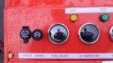 A red control panel featuring gauges for fuel and oil temperature as well as a power outlet and various indicator lights