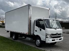 A 2019 Hino 195 box truck with a white cargo area and a silver front is parked on a concrete surface