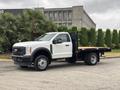 A 2023 Ford F-450 Super Duty truck with a flatbed design and a white exterior parked at an angle