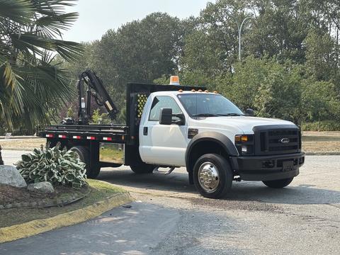 A 2009 Ford F-450 Super Duty with a flatbed and a crane attachment parked with its left side facing the viewer
