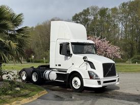 A white 2012 Volvo VNL truck with a sleek design parked with a tall cabin and distinctive grille showcasing its robust build and modern features