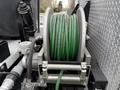 A green hose wound on a metal reel mounted on a vehicle with various hoses and fittings attached to it