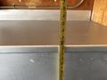 A measuring tape stands upright against a gray metal surface with some dust visible on it