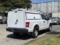 A white 2019 Ford F-150 truck with a utility shell and ladder rack on the bed parked in a lot
