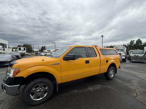 A yellow 2014 Ford F-150 with a cap on the bed and chrome wheels parked on a lot