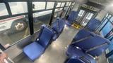 Interior view of a 2021 Ford Transit bus with several blue seats arranged facing each other and safety belts visible