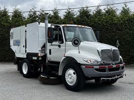 A white 2012 International DuraStar 4300 street sweeper with a large broom attachment at the front and various operational features on the body