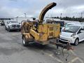 A yellow 2015 Vermeer Corporation BC1200XL wood chipper with a large chute and visible engine components is parked among other vehicles in a lot