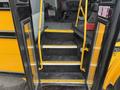 Interior steps of a yellow 2022 Freightliner B2 school bus leading up to the driver's area with black rubber matting and yellow grab rails