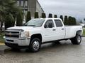 A white 2013 Chevrolet Silverado 3500HD pickup truck with a crew cab and an extended bed is parked on a wet surface