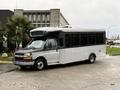 A 2020 Chevrolet Express bus with a black and silver exterior facing slightly to the right parked on a wet surface