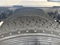 Close-up of a large truck tire with deep tread patterns showing signs of wear and multiple grooves designed for traction