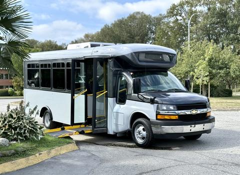 A 2020 Chevrolet Express bus with a black front and white body featuring an open door and a ramp for accessibility