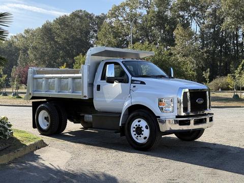 A 2017 Ford F-650 Super Duty dump truck with a white exterior and a silver dump bed parked in a clear area