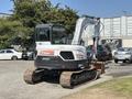 A 2010 Bobcat E80 compact excavator with a cab and arm extended is parked on a gravel surface with tracks and a bucket attachment in the front