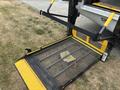 A yellow and black wheelchair lift with a metal grate platform and safety arm extended outward from the back of a van