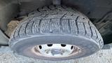 A close-up of a worn tire mounted on a wheel showing visible tread patterns and wear marks