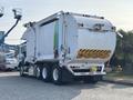 A 2011 Autocar Xpeditor garbage truck with a white body featuring green and blue stripes and a caution sign on the rear