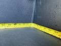 A yellow measuring tape is laid out along the corner of a dark surface measuring various lengths