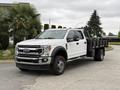 A white 2020 Ford F-550 pickup truck with a flatbed and black sides is parked in a driveway