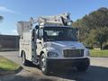 A white 2005 Freightliner M2 106 bucket truck with an elevated platform and utility body parked on a roadway