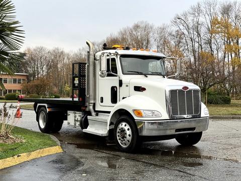 A 2020 Peterbilt 330 flatbed truck with a white exterior silver grille and orange roof lights parked on a wet surface