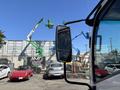 A 2022 Isuzu NRR truck with a side mirror reflecting a construction scene featuring green and yellow lift equipment