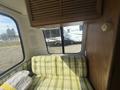 Interior of a 1976 GMC Motorhome featuring green plaid upholstery on a couch and wooden cabinetry above with a window showing the outside view