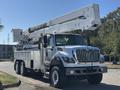 A 2013 International 7500 truck with a white body and an extended aerial lift arm mounted on the back for utility work