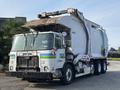 A 2011 Autocar Xpeditor garbage truck with a white cab and side panels featuring blue and green stripes