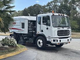 A 2012 Autocar Xpert with a white body and various equipment for street cleaning and maintenance is parked with its side visibly showing an engine compartment