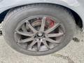 A close-up of a gray alloy wheel with a five-spoke design mounted on a tire featuring prominent lettering and a visible brake caliper in red