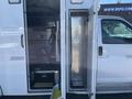 A 2013 Chevrolet Express with an open side door revealing a compartment that contains a driver's seat and storage space
