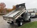 A silver 2015 Ford F-450 dump truck with its bed raised high showing a metal bed interior