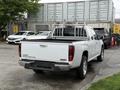 A 2012 GMC Canyon pickup truck with a white exterior and a black bed liner is parked with a ladder rack on the back and has silver alloy wheels