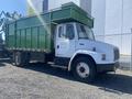 A 1997 Freightliner FL70 truck with a white cab and a green dump bed parked and side view showing its wheels and door with company branding on the side