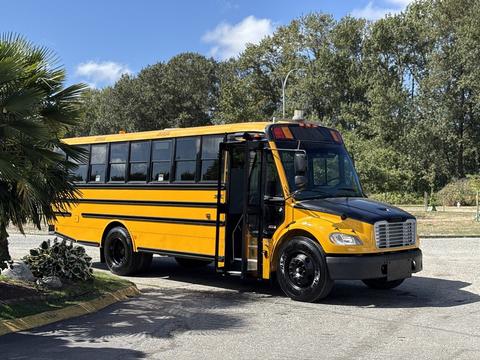 A yellow 2011 Freightliner B2 school bus with a black front bumper and open door parked with its wheels on a concrete surface